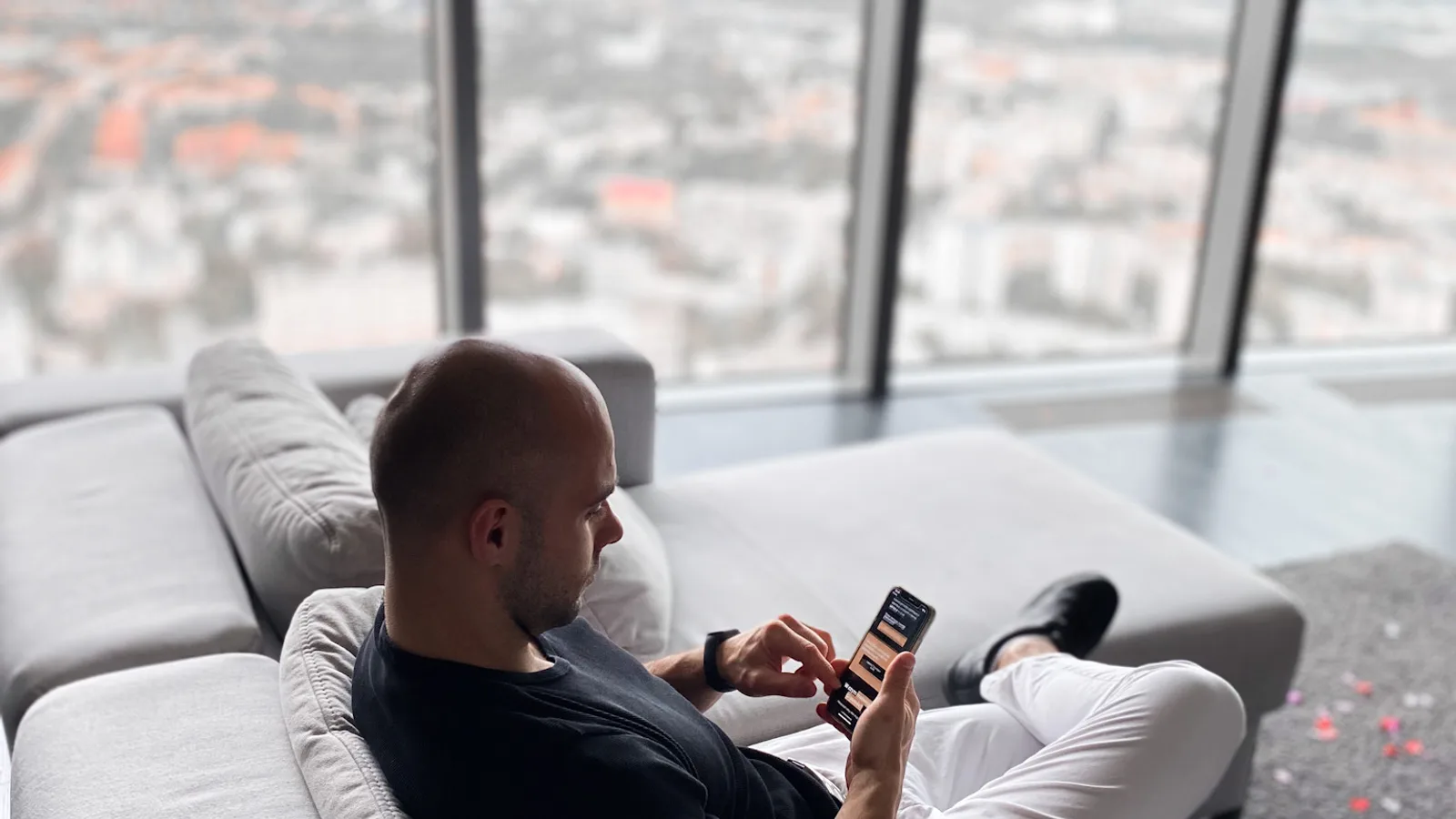 Patryk Borzęcki z telefonem na kanapie, panorama miasta w tle